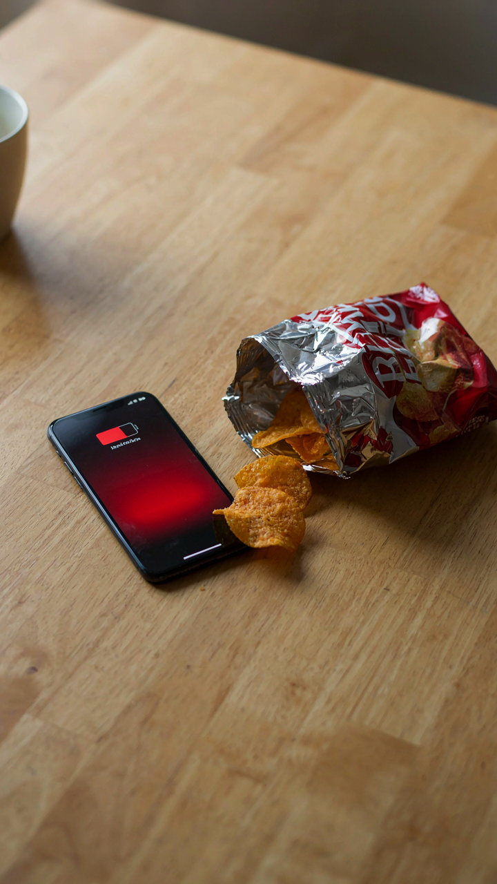 A phone with a low battery sits next to an unhealthy, half-eaten snack.
